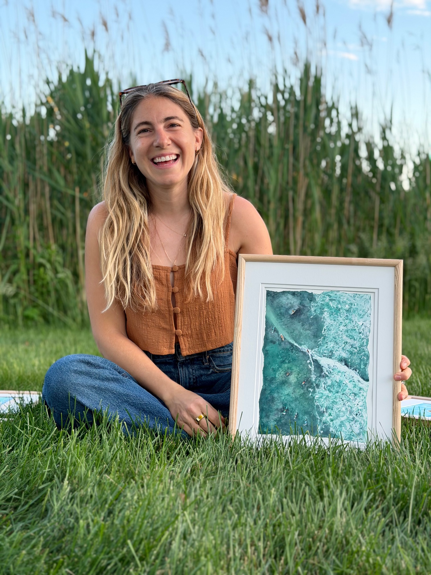 Lynn Moschella in a meadow holding one of her coastal watercolor paintings